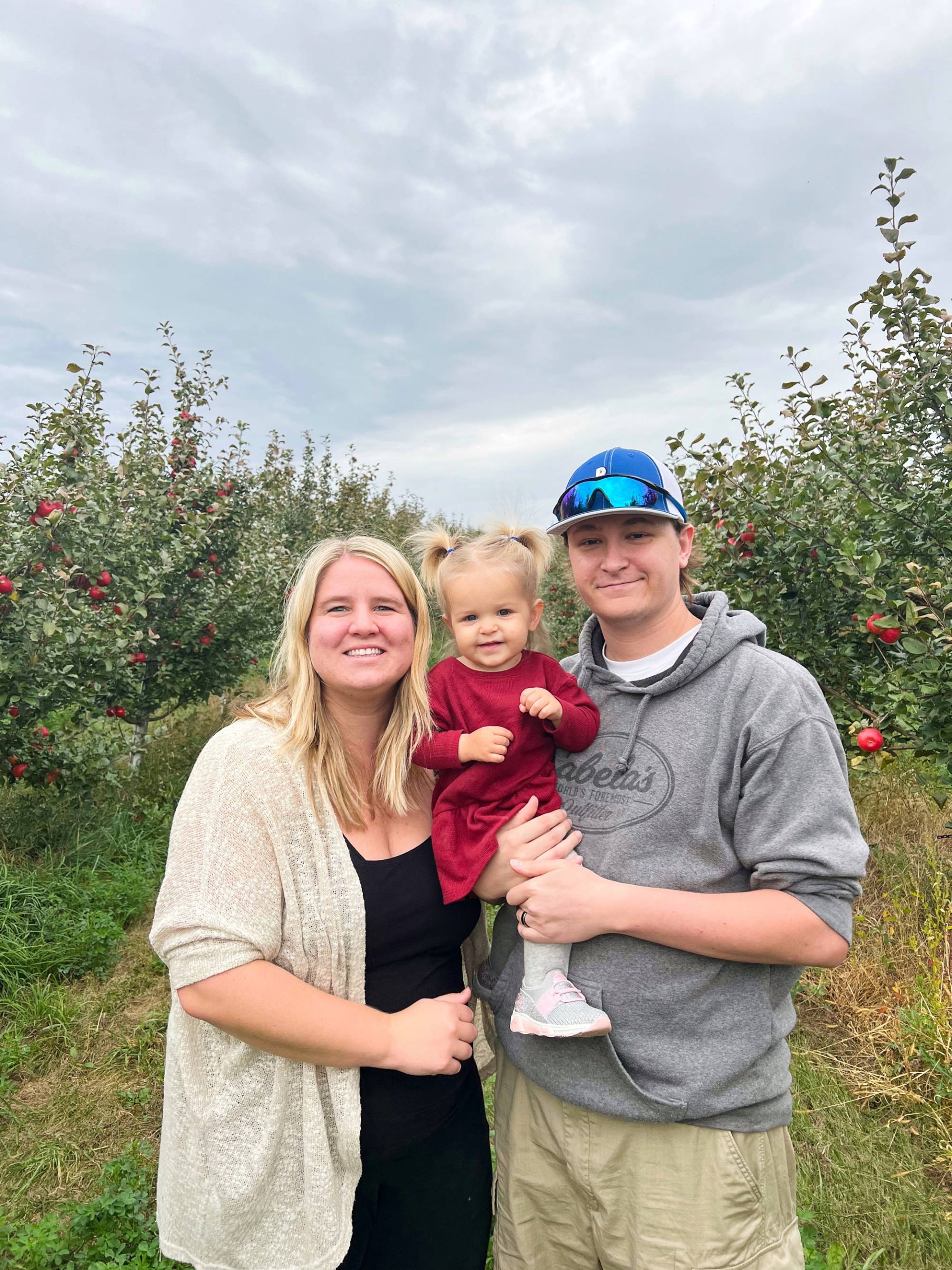 Allie, her husband, and daughter standing in front of apple trees