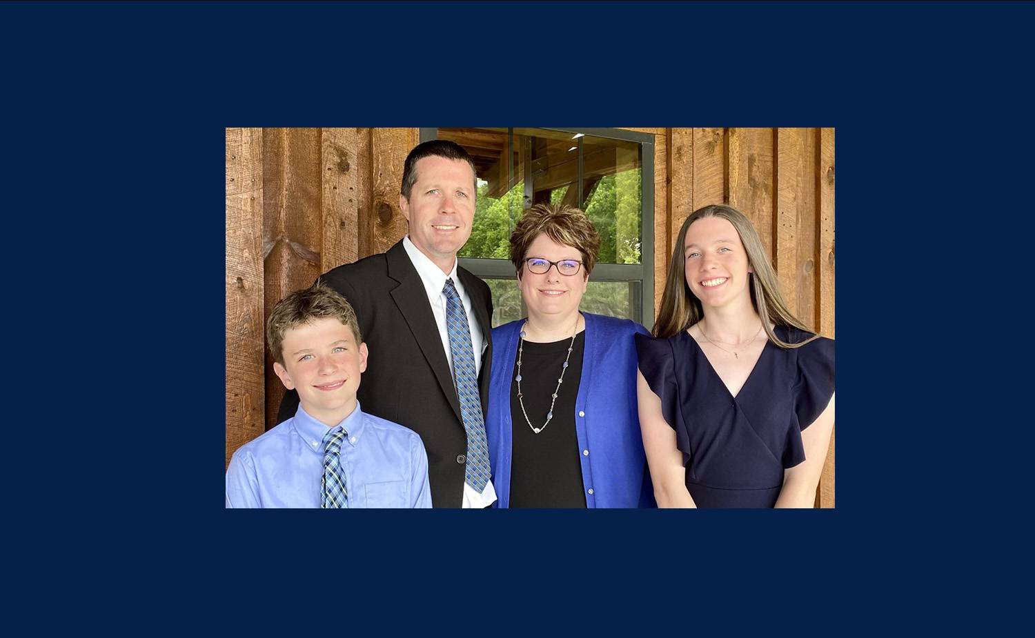 Heather, her husband, daughter, and son standing in front of a wood paneled wall